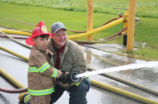 Boy dressed up in firefighter costume holding a hose with a Port Colborne firefighter
