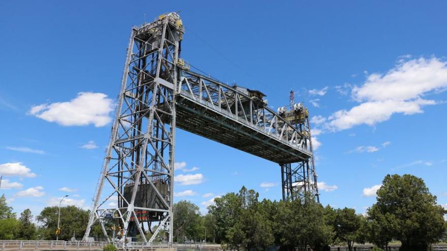 Lift bridge with steel structure, surrounded by greenery and under a clear blue sky.