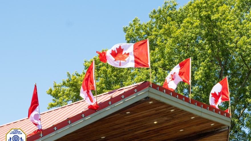 Canadian flags flutter atop a wooden building against a clear blue sky.