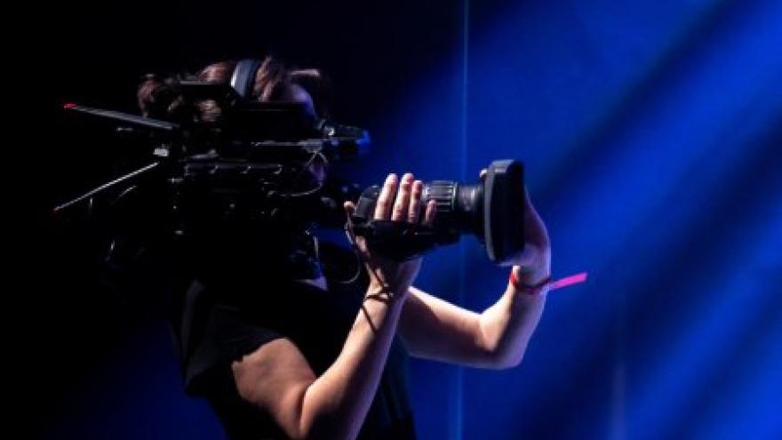 A person holding a camera in a dark setting with blue lighting beams.