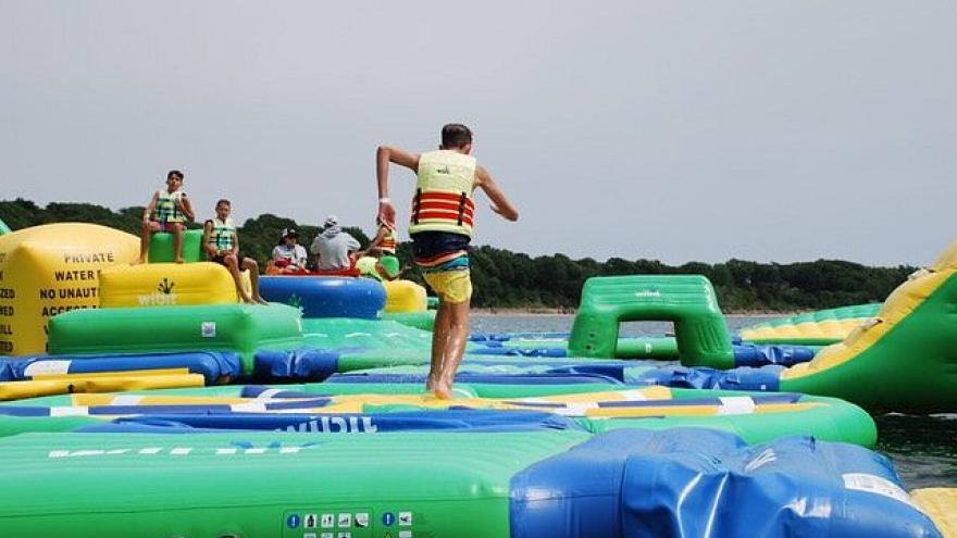 Individuals play on a large, colourful inflatable water obstacle course on a lake.