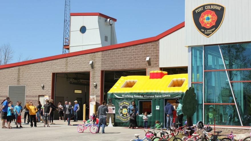 Crowd gathered outside a fire station with a yellow tent and children’s bikes nearby.