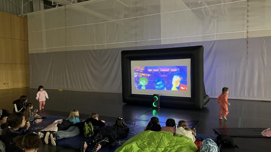 Children seated on the floor watching a cartoon on a large inflatable screen.