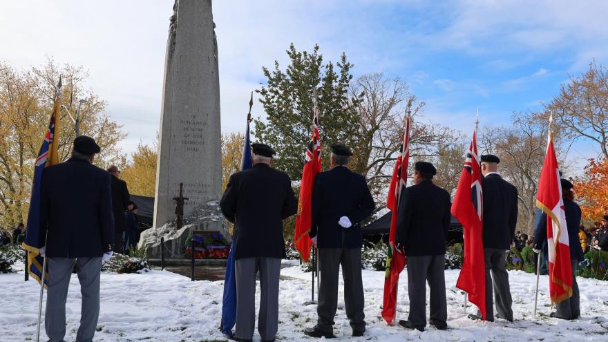 A group of individuals stands in front of a monument, holding flags, in a snowy setting.