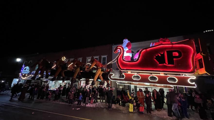 A festive scene at night with a large illuminated sleigh and a crowd of onlookers.