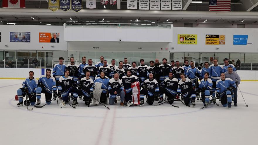 Large group of hockey players posing on ice rink, some in blue jerseys, others in black.