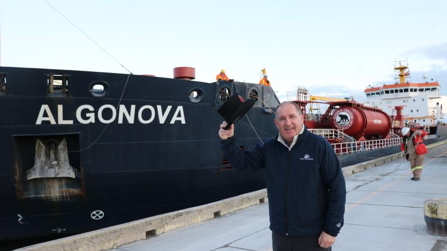 A person waving a hat beside the ship named "ALGONOVA" at a dock.