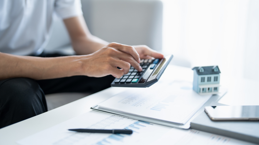 A calculator is being used next to financial documents and a small house model.