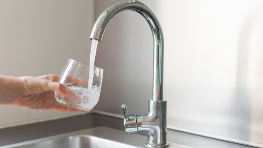 A hand fills a glass with water from a modern kitchen faucet.