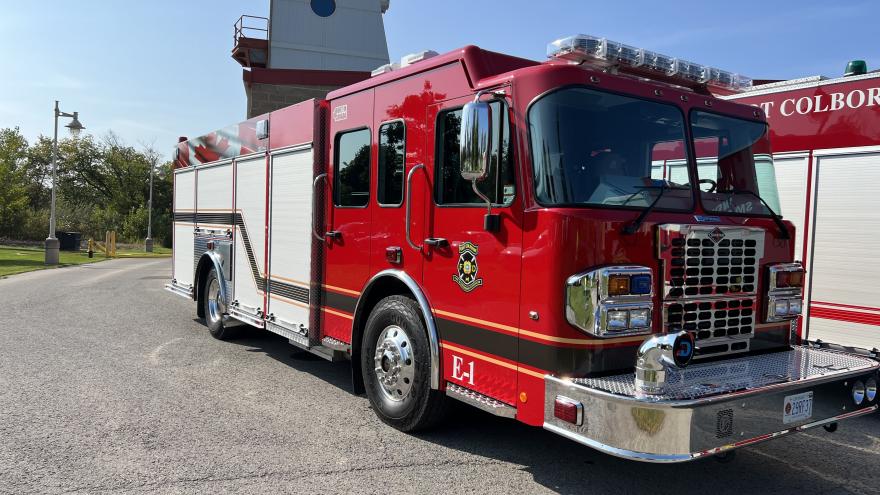 A bright red fire truck parked on asphalt with a fire station in the background.