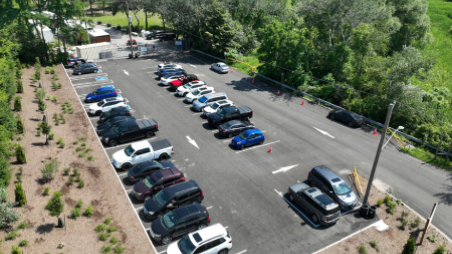 Aerial view of a parking lot with various vehicles and greenery in the background.