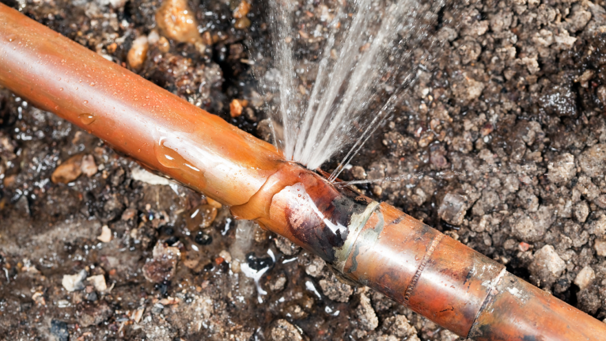 A copper pipe leaking water at a joint, surrounded by dirt.
