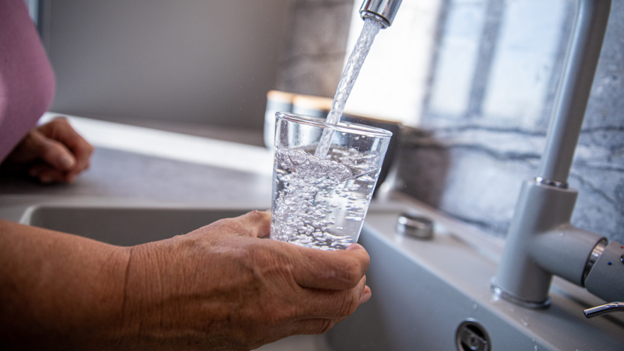 A hand holding a glass while water is poured from a kitchen tap.