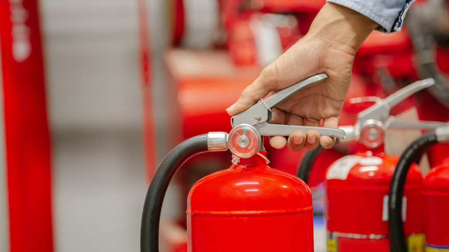 A hand holding the lever of a red fire extinguisher in a storage area.