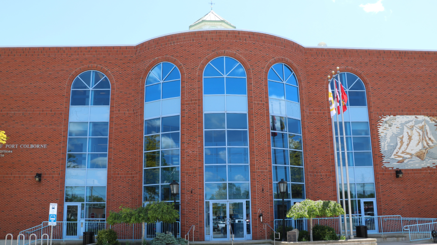 Red brick building with large arched windows and flags in front, under a blue sky.