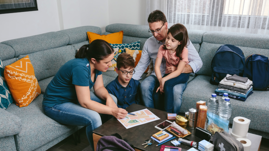 A family gathers on a couch, examining a paper while surrounded by personal items.