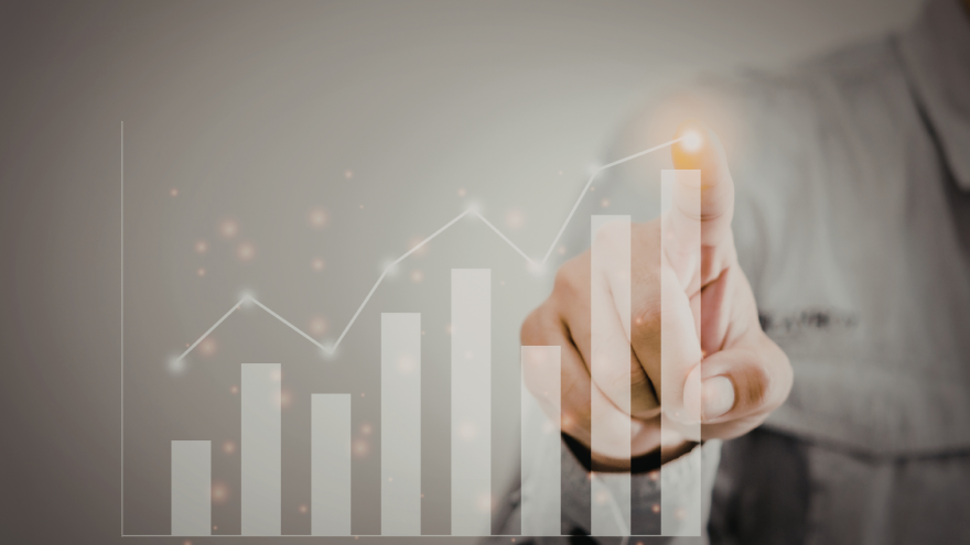A hand points at a rising graph with bars and glowing elements on a grey background.