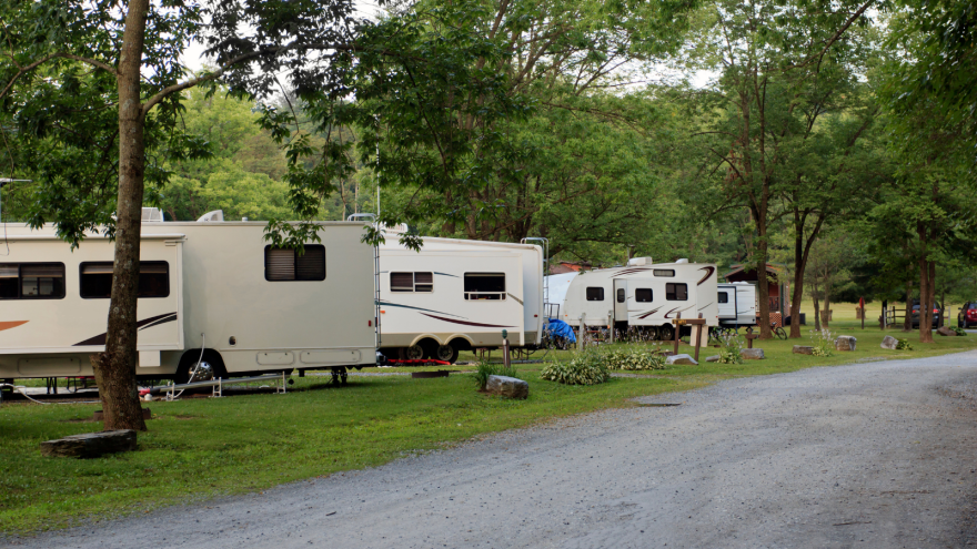 Row of recreational vehicles parked along a gravel path in a green, wooded area.