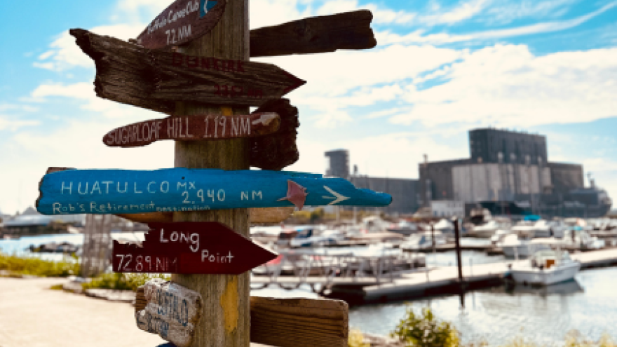 Wooden signpost with directional arrows, boats docked in the background, under a blue sky.