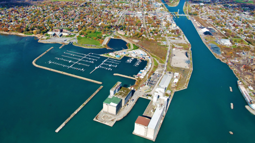 Aerial view of a marina with boats, surrounded by a town and green areas.