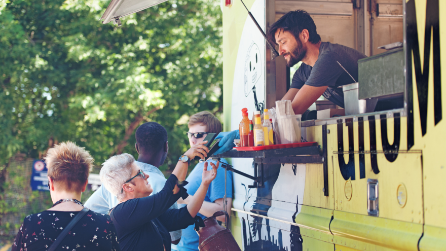 A food truck serving customers outside, with people interacting and a vibrant green background.