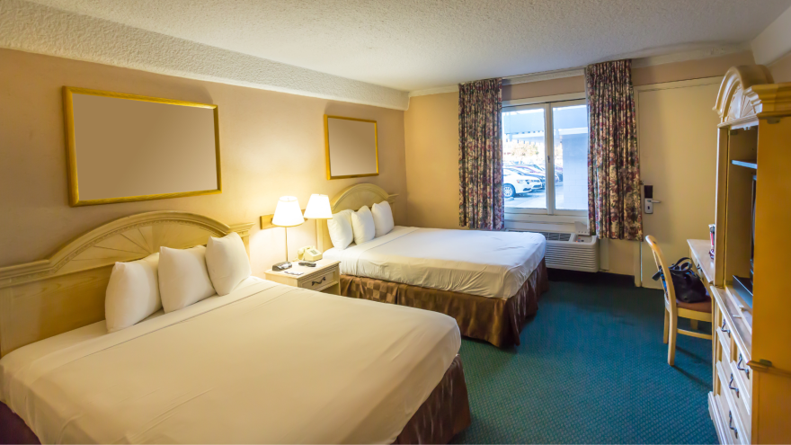 Hotel room with two beds, lamps, and a window, featuring floral curtains.