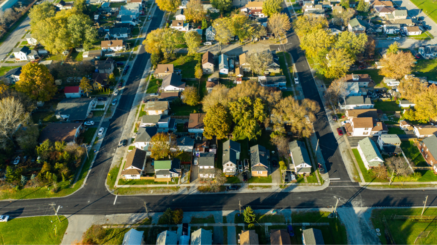 Aerial view of a suburban neighbourhood with trees and houses surrounded by roads.