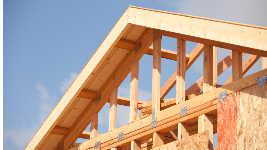 Wooden beams and rafters of a house frame against a clear blue sky.