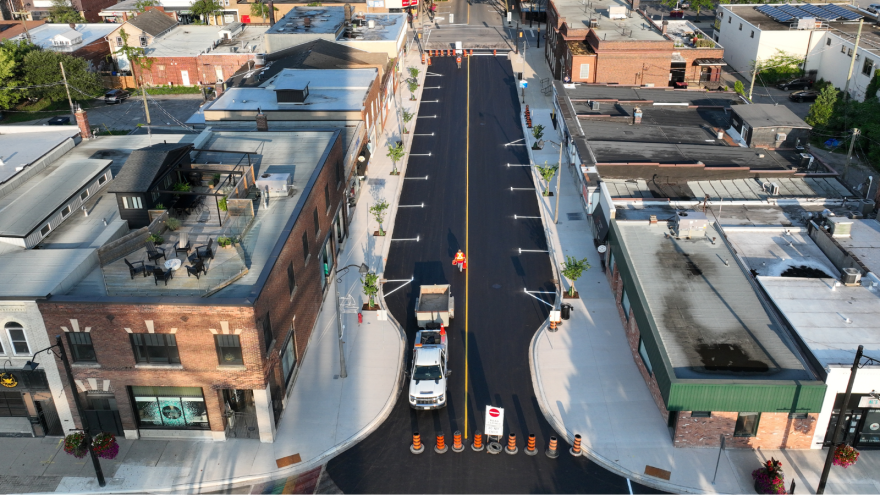 Aerial view of a newly paved street lined with shops and planters, with construction vehicles.