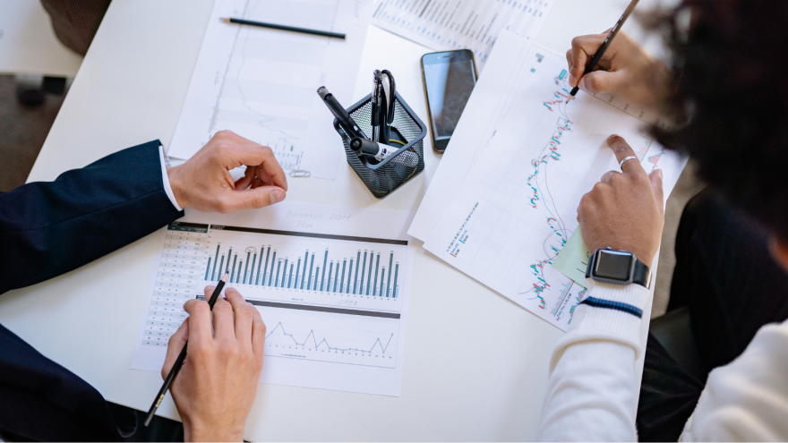 Hands analyzing charts and graphs on a desk, with a pen and digital device.