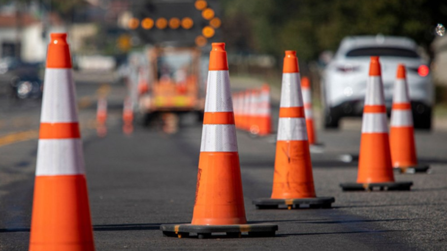 Traffic cones line a road, indicating construction work with blurred vehicles in the background.