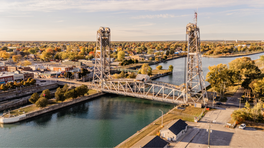 Aerial view of a lift bridge over a calm river, surrounded by autumn foliage and a town.