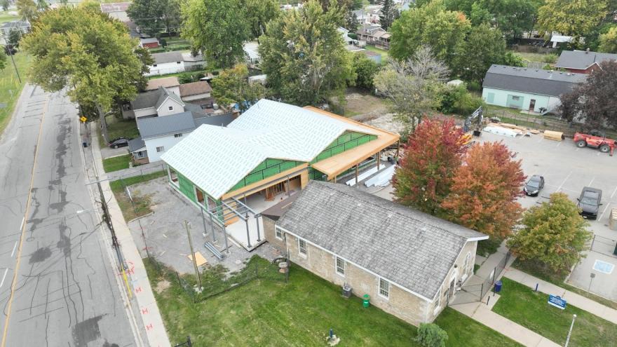 Aerial view of a construction site featuring a new building beside an older structure, surrounded by trees.