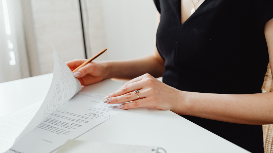 Hands holding documents with a pencil on a white desk, sunlight illuminating the scene.
