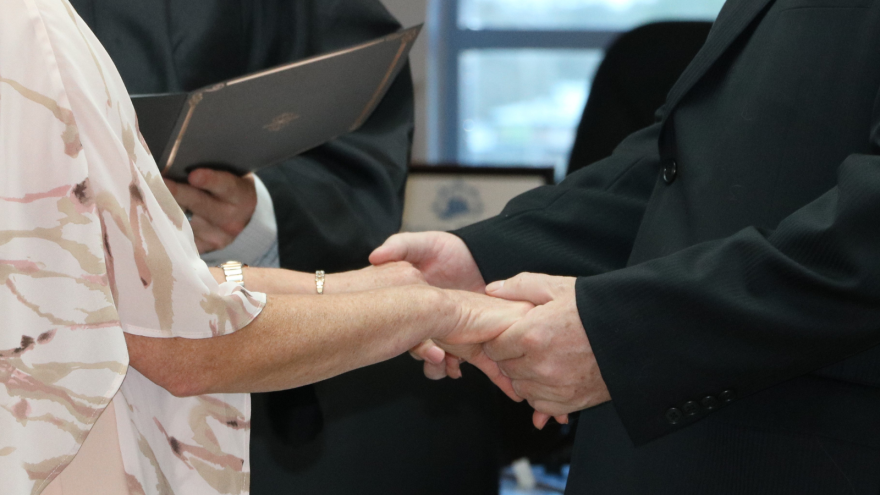 Hands of two individuals clasped together, with a document in the background.