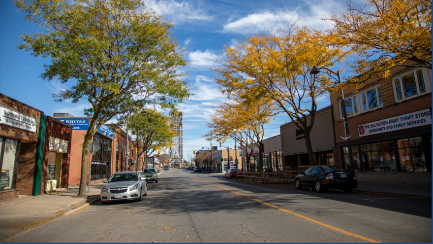Street scene lined with trees showing autumn foliage and stores on either side.