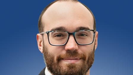 Professional portrait with a person in formal attire, smiling against a blue background.
