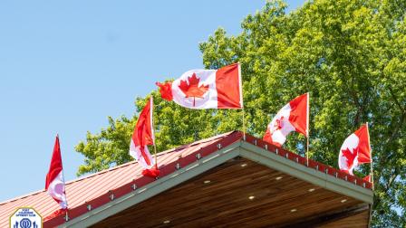 Canadian flags flutter atop a wooden building against a clear blue sky.