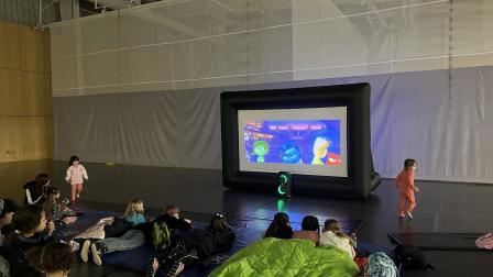 Children seated on the floor watching a cartoon on a large inflatable screen.