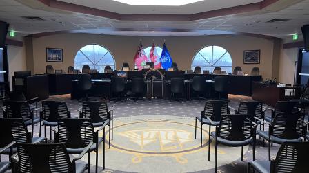 Council chamber with empty chairs, flags, and a circular decorative floor design.