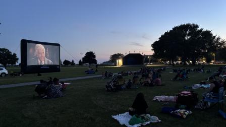 Outdoor movie screening in a park at dusk, with several people watching on blankets.
