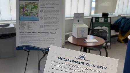 A hand holds a feedback card in front of an information display and a feedback box.