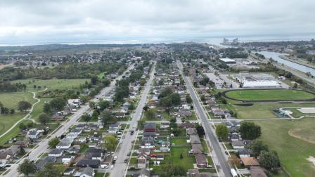 Aerial view of a suburban neighbourhood with houses, roads, and a park under a cloudy sky.