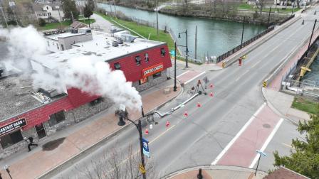 Steam billowing from a building near a road with orange cones and a river in the background.