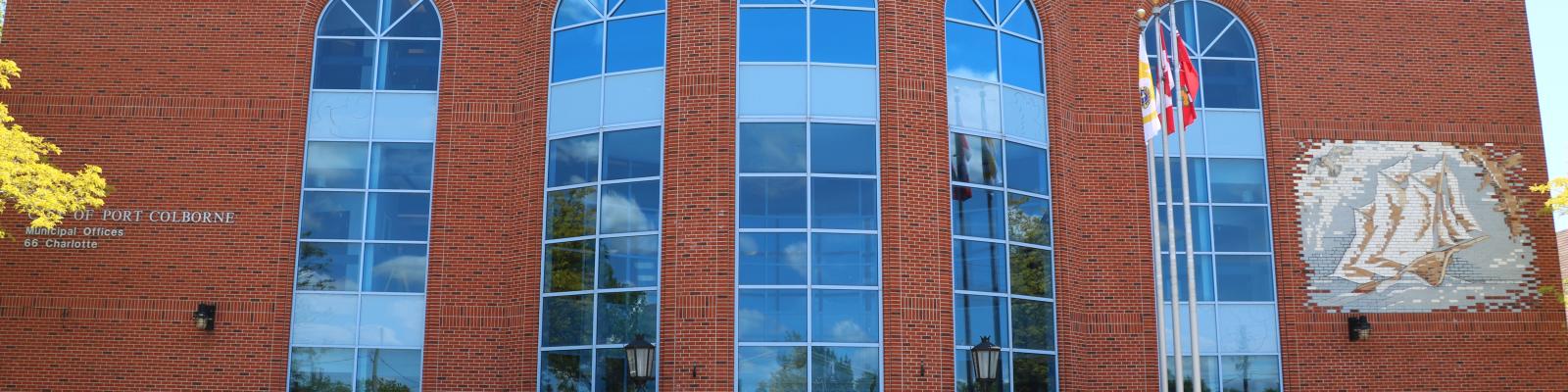 Modern brick building with large glass windows, flags, and a decorative lion sculpture.