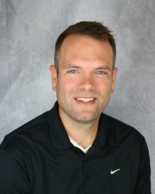Smiling person in a black polo shirt against a grey textured background.
