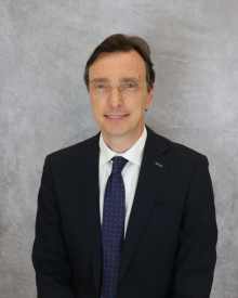 A person in a suit smiles against a grey backdrop.
