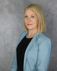 A professional individual in a light blue blazer against a grey backdrop.