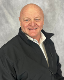 Smiling person in a black jacket against a light grey backdrop.