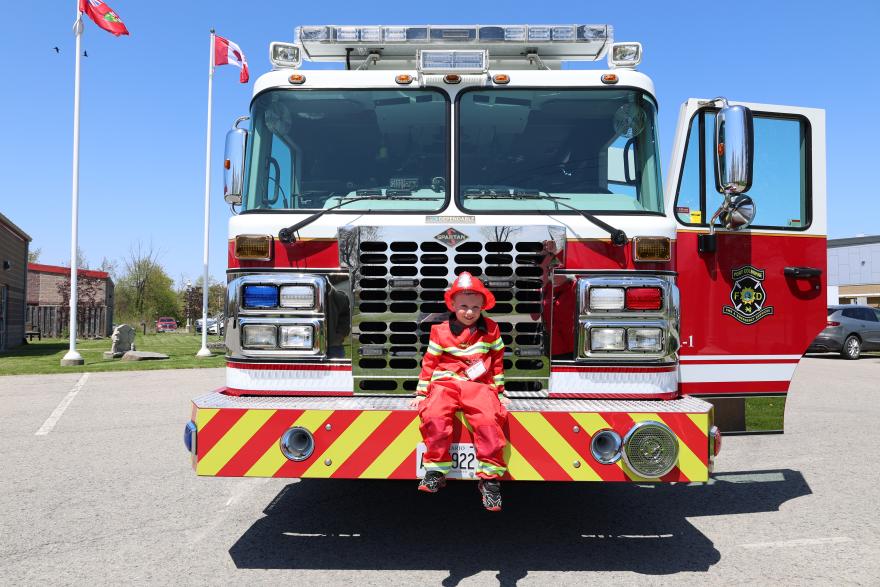A person in a red outfit sits on the front of a fire truck, surrounded by flags.
